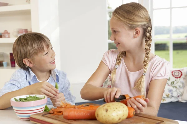 Crianças felizes descascando legumes na cozinha — Fotografia de Stock