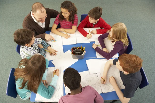 Crianças em idade escolar trabalhando juntas na mesa com o professor — Fotografia de Stock