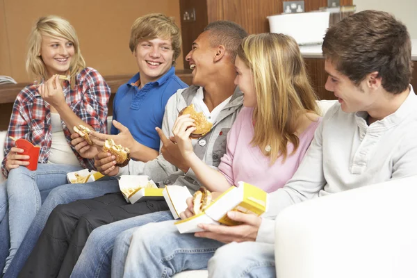Grupp tonåriga vänner sitter på soffan på hem äta snabb foo — Stockfoto
