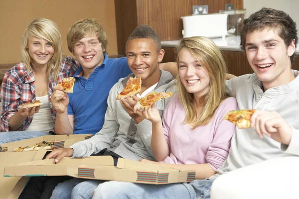 Groep van jeugdvrienden zittend op de Bank op thuis eten pizza — Stockfoto
