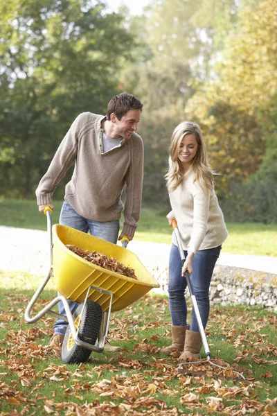 Young couple raking autumn leaves in garden — Stock Photo, Image