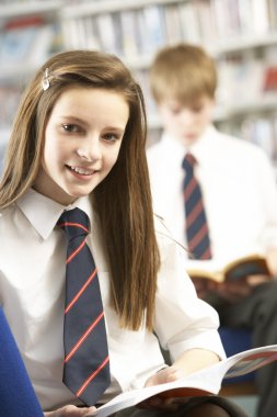 Female Teenage Student In Library Reading Book clipart