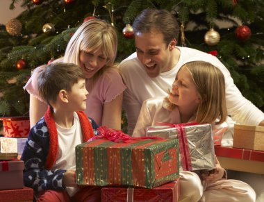 Family Opening Christmas Present In Front Of Tree clipart