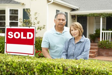 Senior Hispanic couple outside house with sold sign clipart