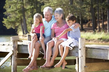 Senior couple sitting by lake with grandchildren clipart
