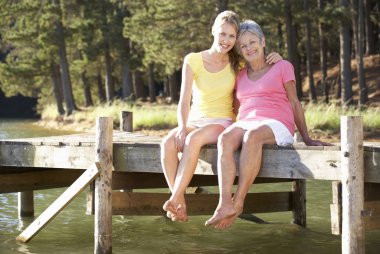 Mother and adult daughter sitting by lake clipart