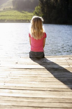 Young girl sitting by lake clipart