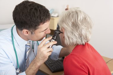 British doctor examining senior woman's ear clipart