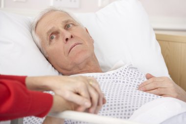 Senior man in hospital bed holding wife's hand clipart