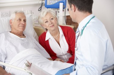 Doctor talking to senior couple on UK Hospital ward clipart