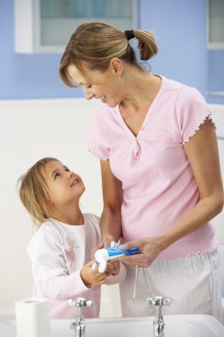 Mother and daughter cleaning teeth in bathroom clipart