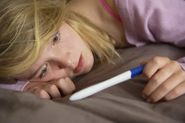 Депрессивная девочка-подросток сидит в спальне с тестом на беременность — стоковое фото