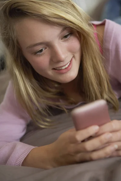 Ragazza adolescente sdraiata in camera da letto utilizzando il telefono cellulare — Foto Stock