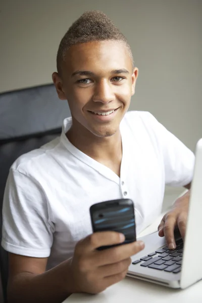 Tonårspojke använder laptop och mobil hemma — Stockfoto