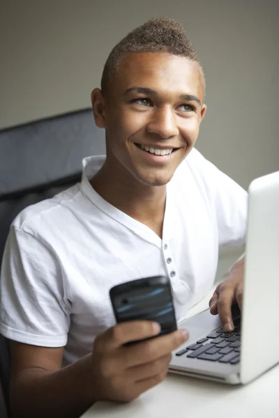Nastoletni chłopiec za pomocą laptopa i telefon w domu — Zdjęcie stockowe