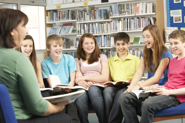 Ученики-подростки в библиотеке читают книги с преподавателем — стоковое фото