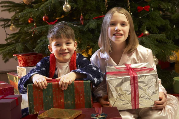 Crianças abrindo o presente de Natal na frente da árvore — Fotografia de Stock