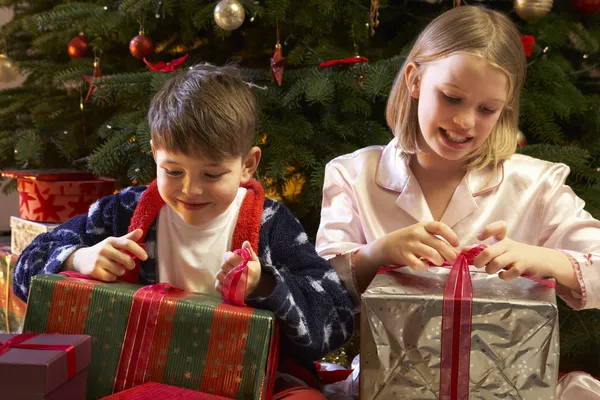 Παιδιά άνοιγμα χριστουγεννιάτικο δώρο μπροστά από το δέντρο — Φωτογραφία Αρχείου