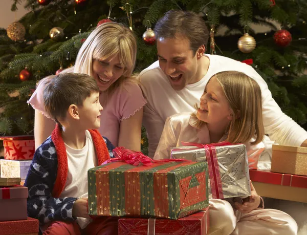 Familj öppnar julklapp framför trädet — Stockfoto