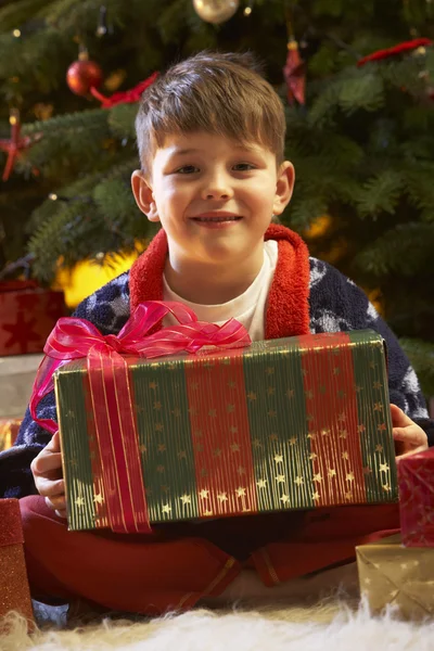 Junge öffnet Weihnachtsgeschenk vor Baum — Stockfoto