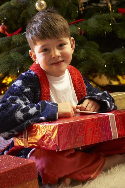 Junge öffnet Weihnachtsgeschenk vor Baum — Stockfoto