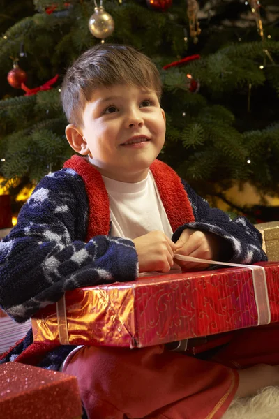 Jovem menino abrindo presente de Natal na frente da árvore — Fotografia de Stock