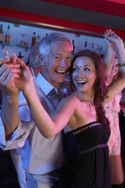 Hombre mayor bailando con una mujer más joven en un bar ocupado — Foto de Stock