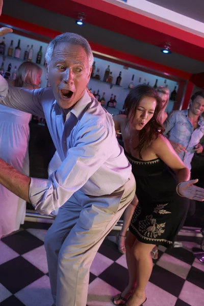 Starší muž tančí s mladší ženou v rušný bar — Stock fotografie