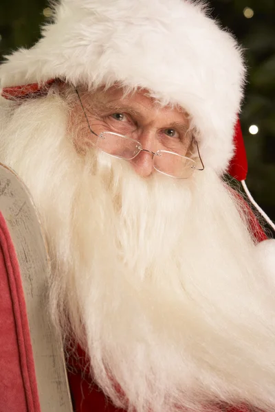 Санта-Клаус сидит в кресле перед елкой — стоковое фото