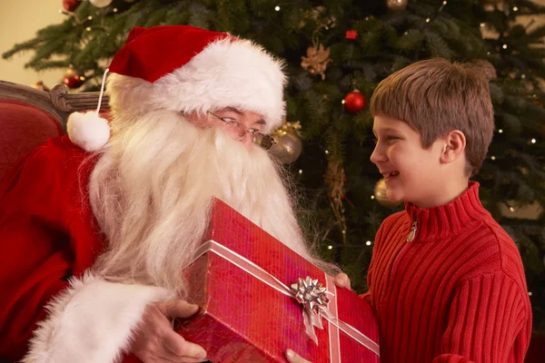 Babbo Natale che fa un regalo al ragazzo davanti all'albero di Natale — Foto Stock