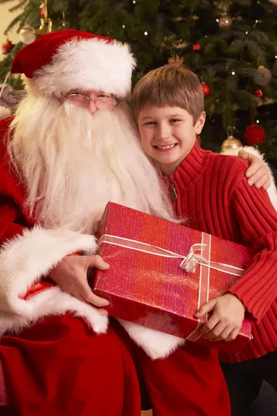 Papai Noel dando presente para menino na frente da árvore de Natal — Fotografia de Stock