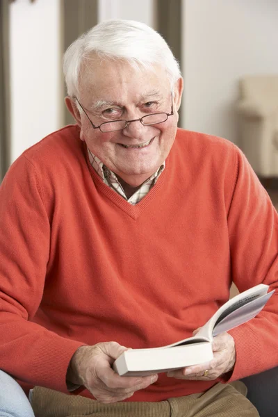 Hombre mayor que relaja en silla en el libro casero de la lectura —  Fotos de Stock