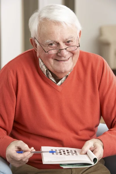 Senior man ontspannen in stoel thuis voltooiing kruiswoordraadsel — Stockfoto