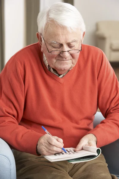 Senior man ontspannen in stoel thuis voltooiing kruiswoordraadsel — Stockfoto