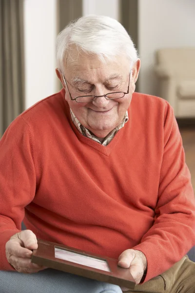 Senior mannen tittar på fotografiet i ram — Stockfoto