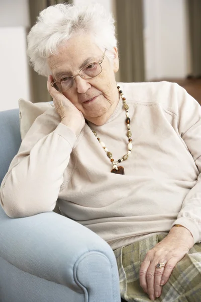 Äldre kvinna söker sorglig i stol hemma — Stockfoto