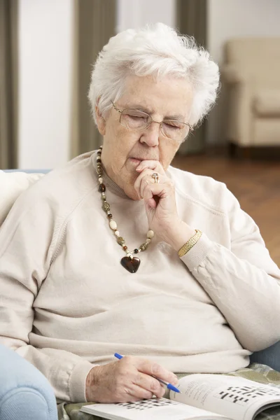 Seniorin entspannt im Stuhl zu Hause beim Kreuzworträtsel — Stockfoto