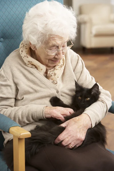 Äldre kvinna avkopplande i stol hemma med husdjur katt — Stockfoto