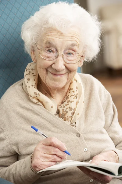 Mujer mayor relajándose en silla en casa completando crucigrama —  Fotos de Stock