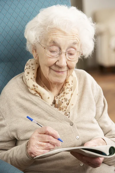 Femme âgée se détendre dans la chaise à la maison Terminer mot croisé — Photo