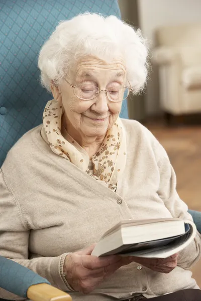 Senior vrouw ontspannen in stoel thuis leesboek — Stockfoto