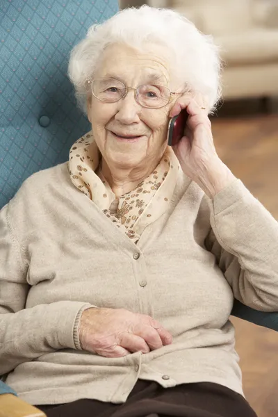 Starszy kobieta rozmowy na telefon komórkowy siedząc w fotelu w domu — Zdjęcie stockowe