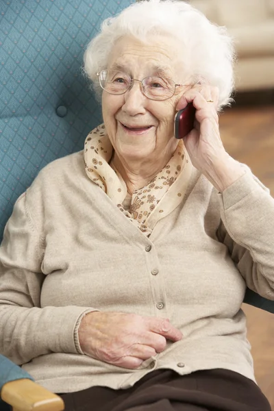 Senior mulher falando no telefone móvel sentado na cadeira em casa — Fotografia de Stock