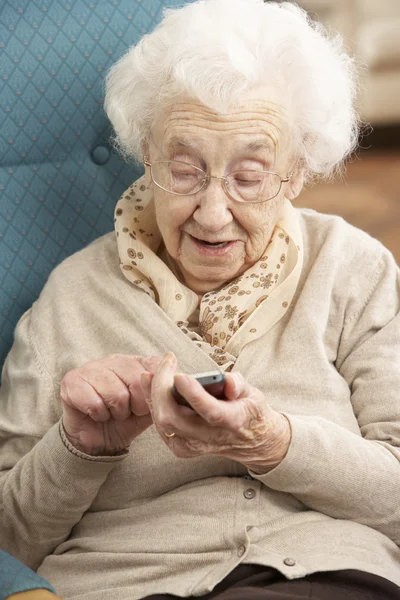 Äldre kvinna ringa numret på mobiltelefon sitter i stol på — Stockfoto