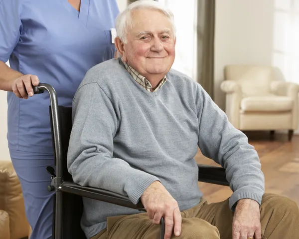 Senior man zit in rolstoel met verzorger achter uitgeschakeld — Stockfoto
