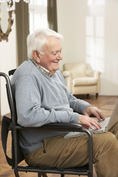 Hombre mayor discapacitado sentado en silla de ruedas usando computadora portátil —  Fotos de Stock