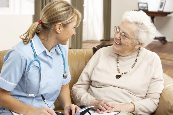 Äldre kvinna i diskussion med hälsa besökare hemma — Stockfoto