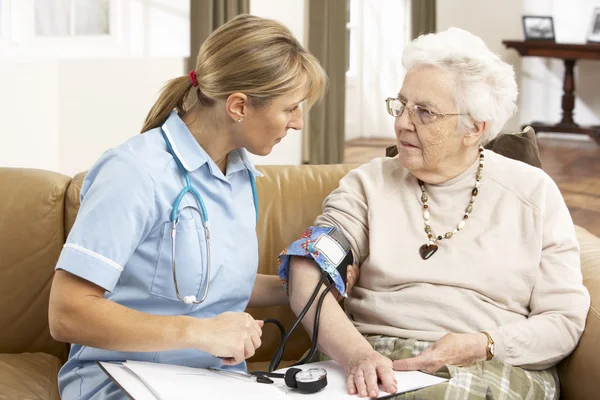 Donna anziana che si comporta pressione sanguigna presa dal visitatore di salute a H — Foto Stock
