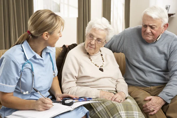 Äldre par i diskussion med hälsa besökare hemma — Stockfoto