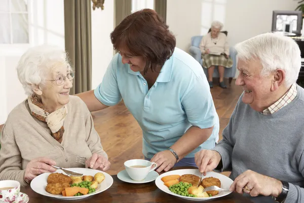 Senior koppel maaltijd wordt geserveerd door verzorger — Stockfoto